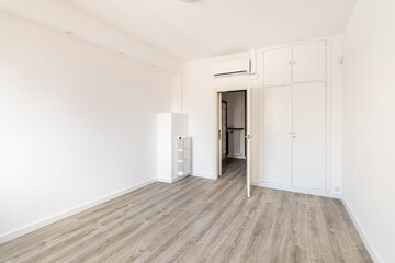 An empty spacious room for a bedroom, with a closet built into the wall, an air conditioner above the front door and a radiator on the wall to create heat during the cold season. Eco wood floor.