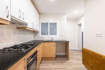 Modular furniture in kitchen with white cabinets on top of wall and cabinets with wood doors below. Black worktop with gas stove. On wall opposite, there is folding solid wood tabletop to save space.