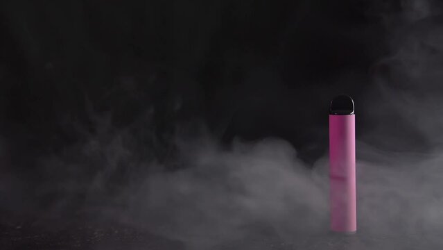Pink electronic cigarette vape on dark background with smoke. High quality photo