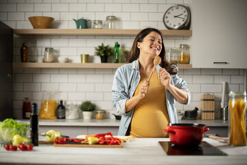 Beautiful pregnant woman preparing delicious food. Smiling woman having fun while cooking at home.