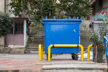 A blue trash can behind a yellow railing.