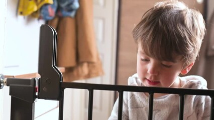 little boy standing on the other side of the child safety gate and holding on to the top of the security gate. Alone at home without parental advisory. Selected focus