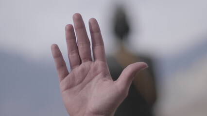 Female open hand with huge Buddha statue in the background.