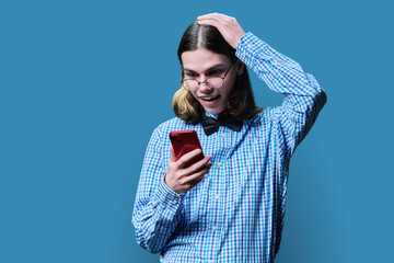 Joyful surprised young male looking in smartphone, on blue background