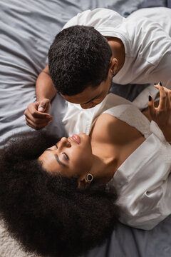high angle view of african american woman with sexy breast and closed eyes lying on bed near young boyfriend