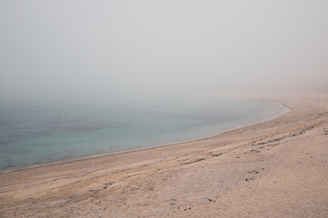 Sandy beach in heavy fog without people. The water is turquoise in color.