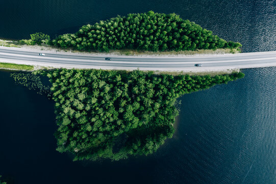 Aerial view of road through blue lakes with green woods in Finland.