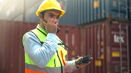 Logistic staff flying drone to survey and inspect stack container in shipment company area. 
