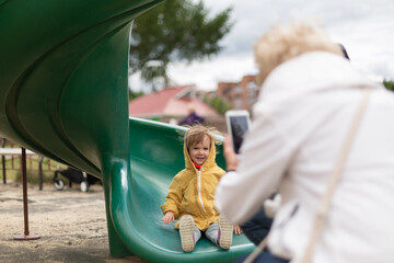 Grandmother taking pictures of her granddaughter going down the slide