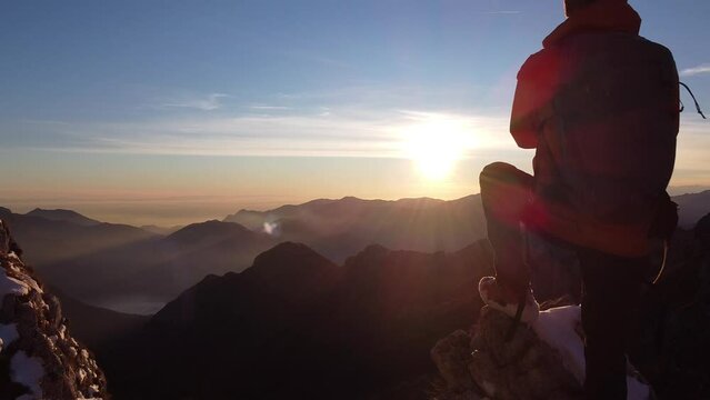 Hiker standing on snowy mountain top during sunset
