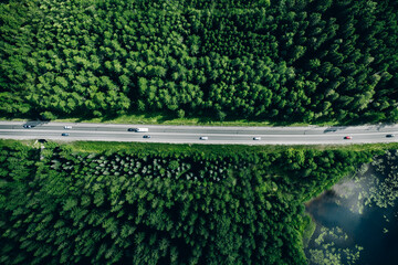 Aerial view of road with cars through green summer woods by blue water lake in Finland.