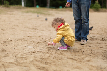 Little girl drawing on sand  with her father