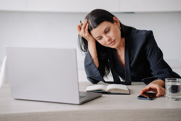 Exhausted brunette American businesswoman sitting at desk with laptop, diary, phone leaning on hand. Overworked caucasian sleepy female lawyer tired, feels fatigue. Business, finance. Remote work.