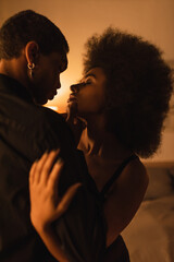 seductive african american woman with closed eyes hugging young man in dark room with lighting