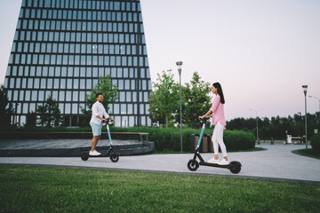 Cheerful diverse couple riding kick scooters on street