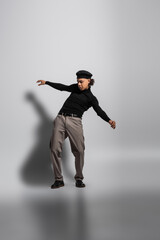 Fototapeta na wymiar full length of young and stylish african american guy in black beret and turtleneck with pants posing on grey background