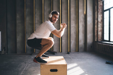 Confident sportsman doing squats on jump box in modern gym