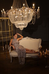 Portrait of young porsh woman in gorgeous dress of stones. Beautiful lights of big low chandelier....