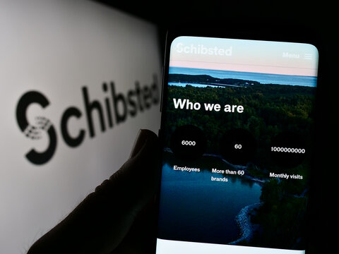 Stuttgart, Germany - 01-28-2023: Person holding cellphone with website of Norwegian company Schibsted Media Group on screen in front of logo. Focus on center of phone display.