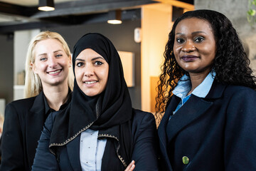 Smiling business women with different ethnicities and cultures looking at camera in modern office -...