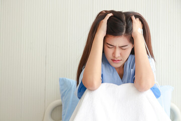 Naklejka premium Stressed Asian female patient holding her head in a hospital bed. Taking out health insurance. women's health problems
