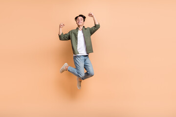 Fototapeta na wymiar Full length size cadre of young jumping carefree overjoyed handsome guy fists up champion jump trampoline positive isolated on beige color background