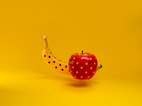 Close-up of an apple and banana painted with polka dots against a yellow background