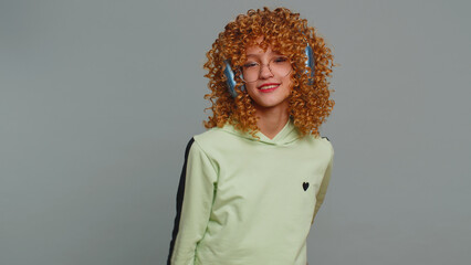 Happy child girl kid listening music on headphones, dancing disco fooling around having fun expressive gesticulating hands, relaxing. Teenager curly haired children isolated on studio gray background