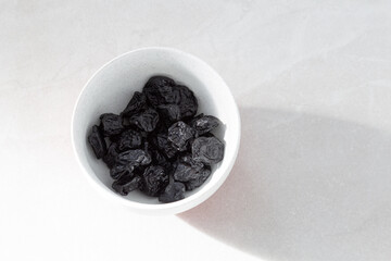 Selective focus flat lay side lit view of pitted dried prunes in lightly speckled white bowl on...