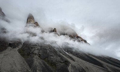 Scienic landscape with rocky mountain top in low clouds in gray cloudy sky. Akshayuk Pass, Baffin Island mountain seen through clouds. mountains background