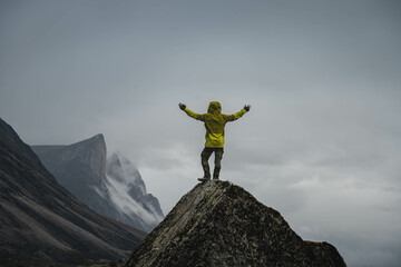 A man standing on a stone cliff in Akshayuk Pass, Nunnavut, Canada. Foggy mountains, cloudy morning...