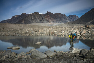Hiker walking through remote arctic valley Akshayuk Pass, Baffin Island, Canada . Dramatic arctic...