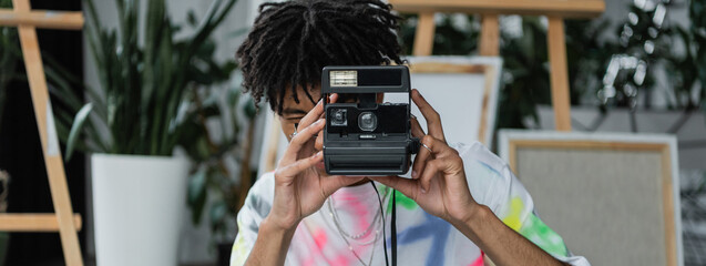 Young african american artist taking photo on vintage camera in studio, banner.
