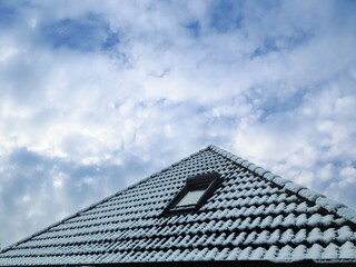 Open roof window in velux style with black roof tiles covered in white snow