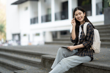 Asian college student using tablet for her university project while sitting in front of the class building.