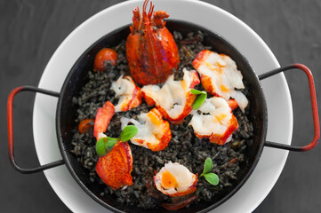 Close-up of solo paella with lobster slices, tomatoes, squid ink sauce, herbs, and saffron. Hot...