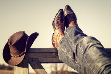 Cowboy boots and hat with feet up resting with legs crossed - 567771597