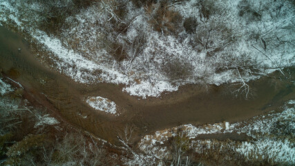 Looking down at a snowy Creek in a forest Valley from a birds eye view during winter
