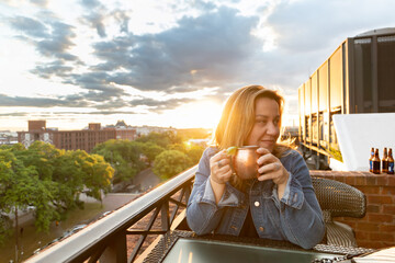 a single woman in her 40's wearing a denim jean jacket enjoying a mule cocktail looking away