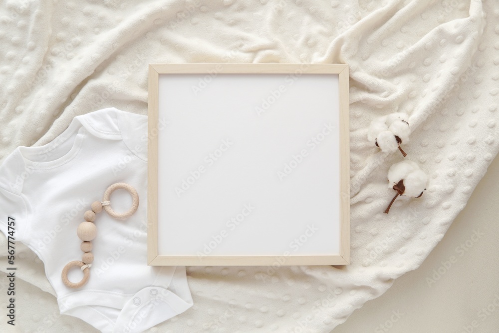 Wall mural Flat lay with blank square wooden frame on baby blanket, mockup for nursery art or pregnancy announcement.