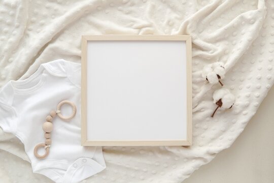 Flat lay with blank square wooden frame on baby blanket, mockup for nursery art or pregnancy announcement.
