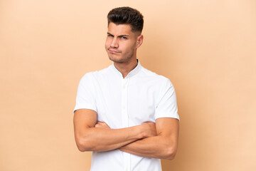 Young caucasian man isolated on beige background with unhappy expression