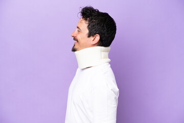 Obraz premium Young caucasian man wearing neck brace isolated on purple background looking side