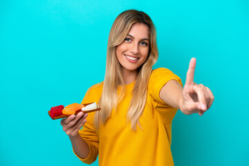 Obraz premium Young Uruguayan woman holding sashimi isolated on blue background showing and lifting a finger