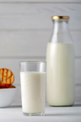Glass and bottle of milk on a white wooden background.