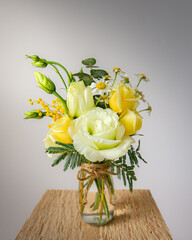 Bouquet of wildflowers in a small glass vase on wood plank. Soft pastel yellows and greens. Jute string bow. Spring season  photography. Shadows on the white wall. Country style, Farmhouse, handmade