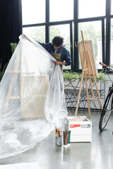 Obraz na płótnie Canvas African american artist putting cellophane on easel in studio.