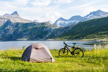 Fjord and mountain landscape in Norway with bike and tent on a grassland in the foreground