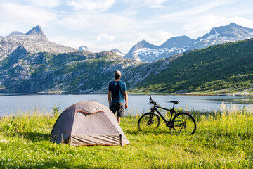 Man standing next to his trekking tent and bike on a bike travel through Norway with fjord and...
