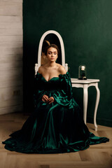 Fototapeta premium a girl in a green dress sitting against the background of a wall and a mirror